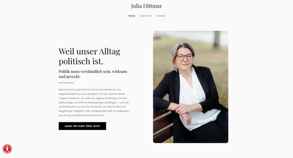 Julia Dittmar, eine Kandidatin für das Abgeordnetenhaus, sitzt lächelnd auf einer Parkbank, trägt eine Brille und einen schwarzen Blazer über einer weißen Bluse. Sie ist eine Kandidatin für das Abgeordnetenhaus von Berlin.