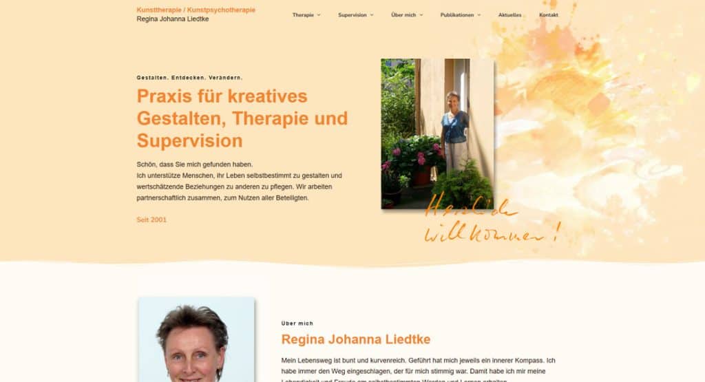 Regina Johanna Liedtke lächelt warm vor üppig blühenden Pflanzen in einem sonnigen Innenhof, einladend für kreatives Gestalten, Therapie und Supervision.