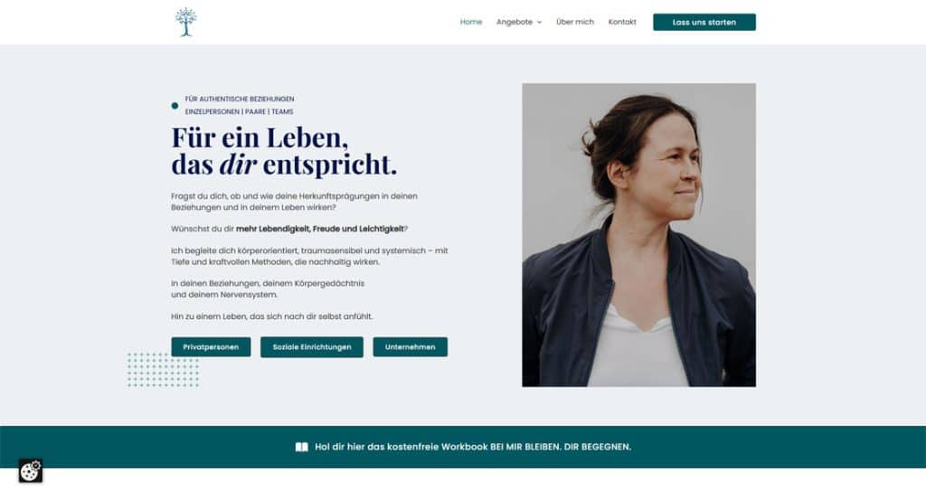 Eine Frau mittleren Alters mit schulterlangem braunem Haar blickt nach rechts und lächelt leicht. Sie trägt eine dunkelblaue Jacke über einem cremefarbenen Oberteil. Im Hintergrund ist ein Ausschnitt eines dunklen, modernen Outfits zu sehen.